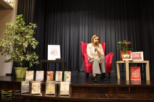 Sabina Waszut na scenie w fotelu, obok wystawione jej książki