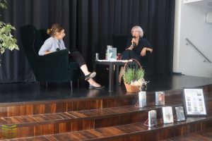 Lidia Czyż i dyrektorka biblioteki Ilona Majewska, na scenie, rozmawiają.