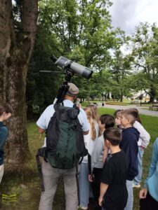 Autor z młodzieżą w parku, na ramieniu luneta ze statywem.